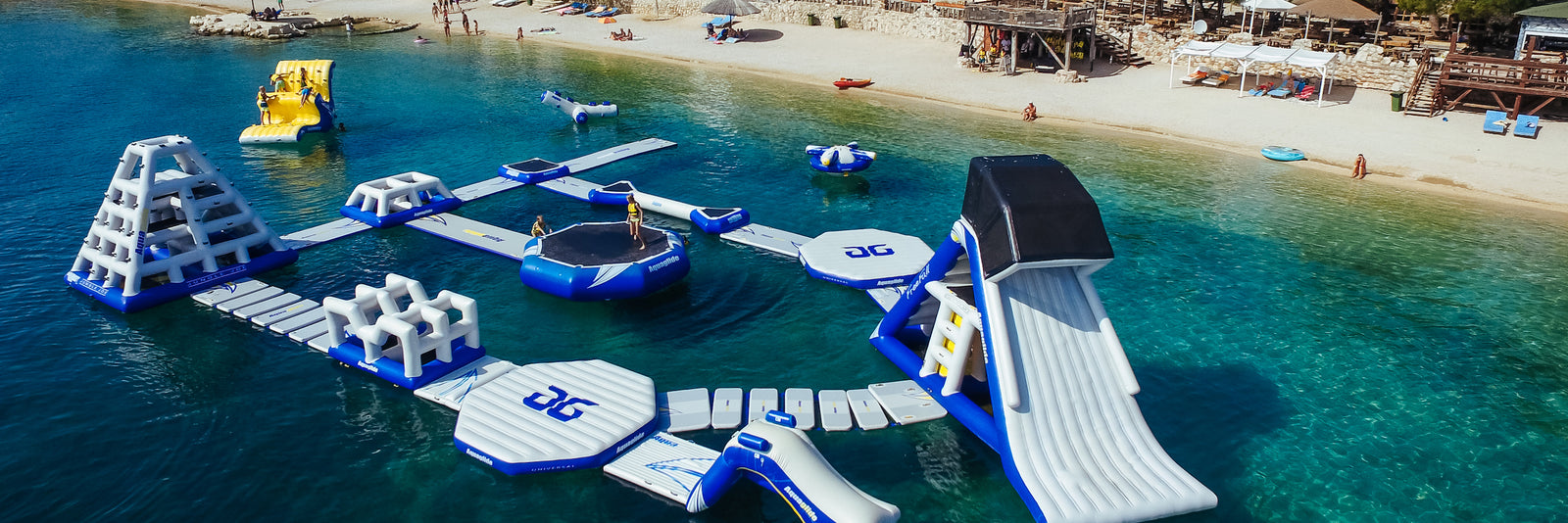 Large Aquaglide floating water park bear the shore of a lake with multiple kids playing on the slides and other obstacles.