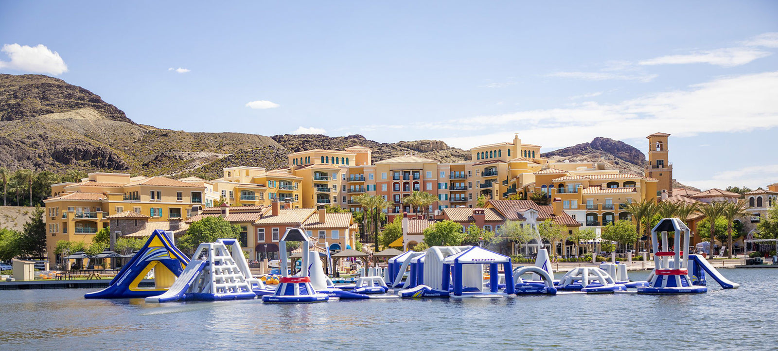 Floating water park on a lake with colorful resort buildings in the background.
