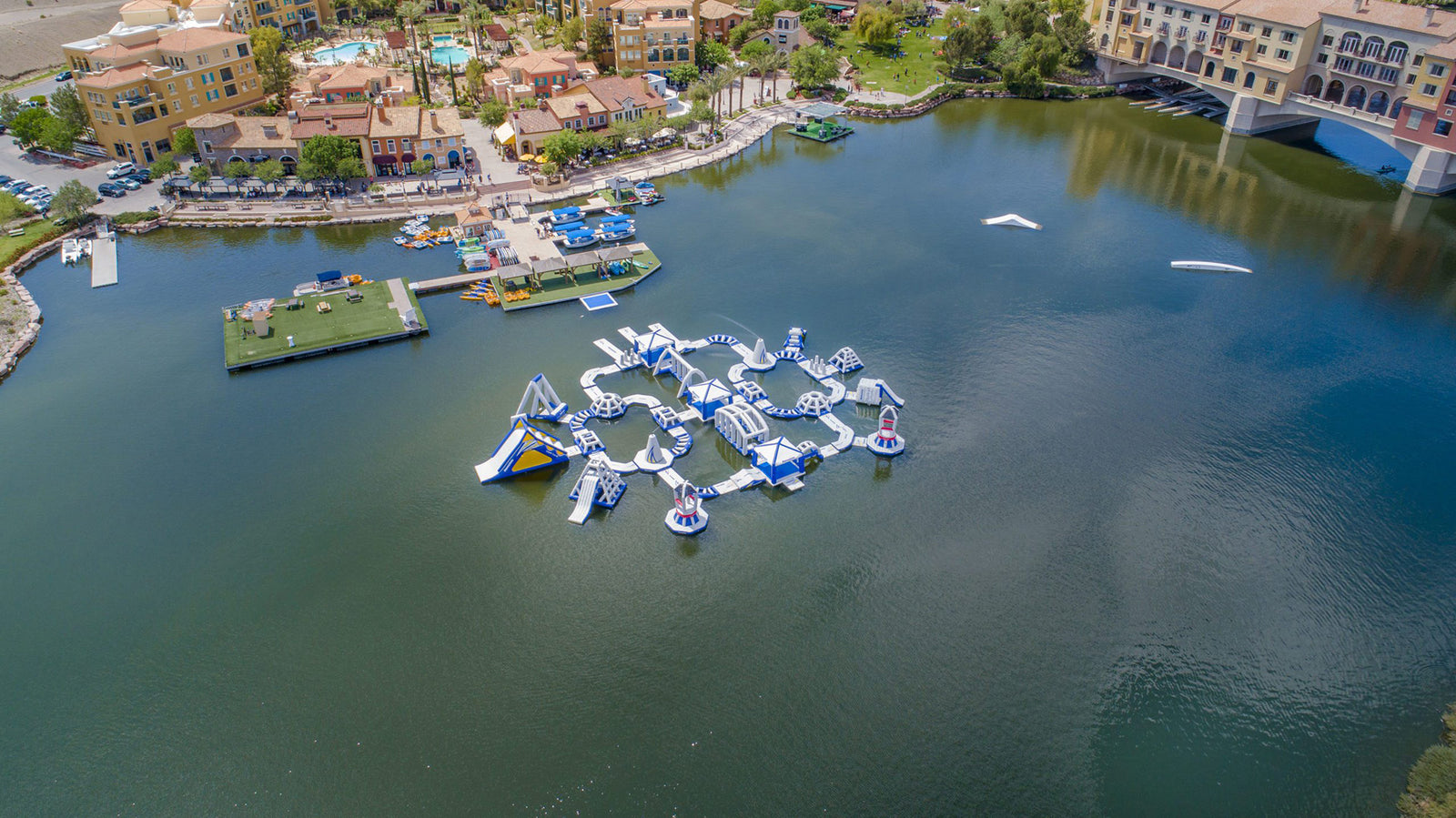 Aerial view of a water park with inflatable obstacles on a lake near a resort town.