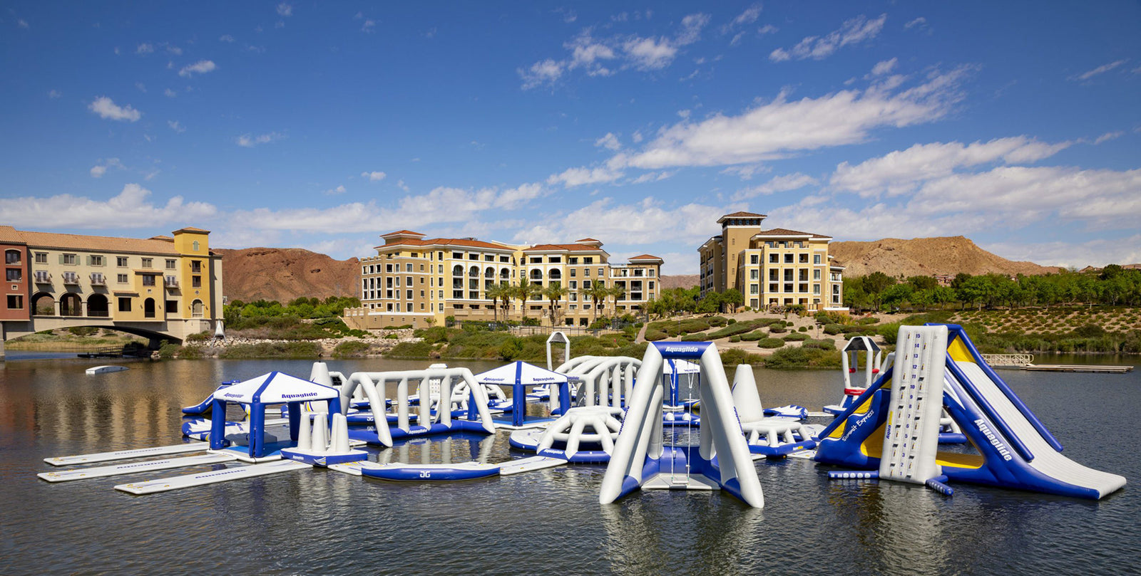 Floating obstacle course on a lake with buildings and hills in the background.