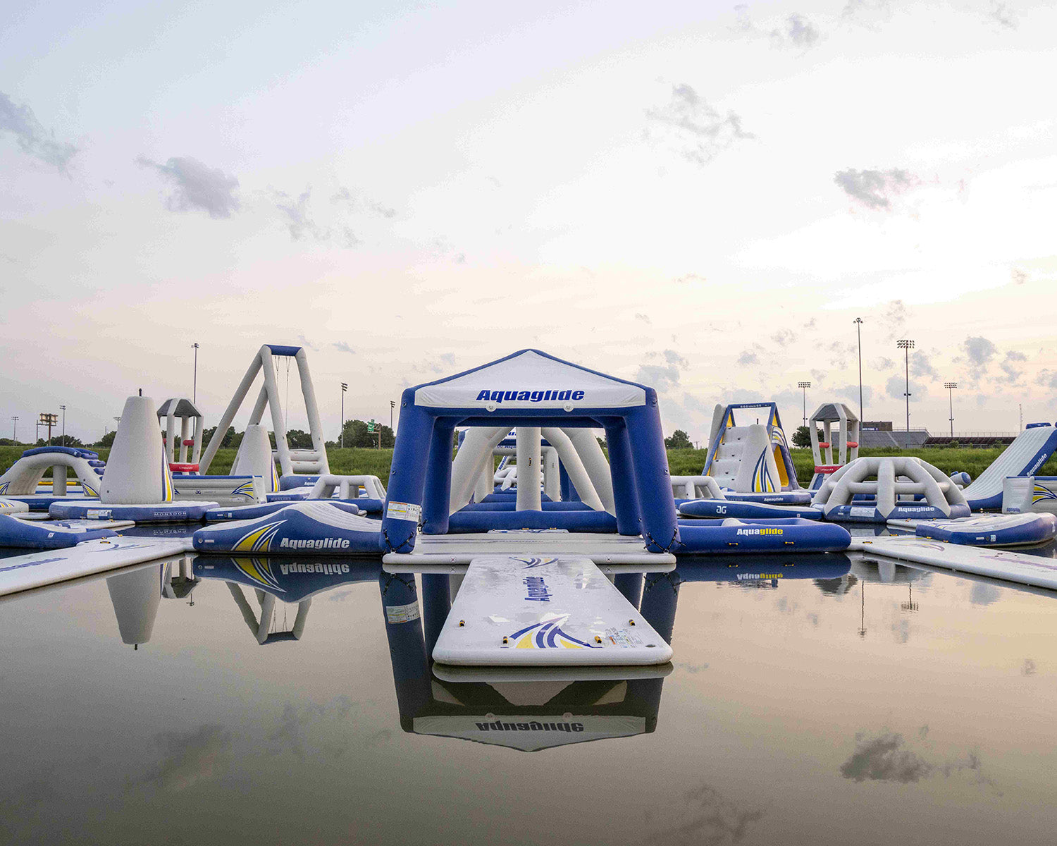 Inflatable water obstacle course on a calm lake under a cloudy sky.