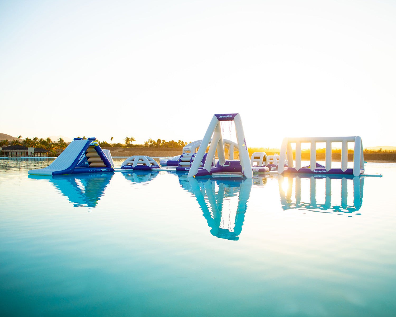 Inflatable water park floats on a calm lake at sunrise.