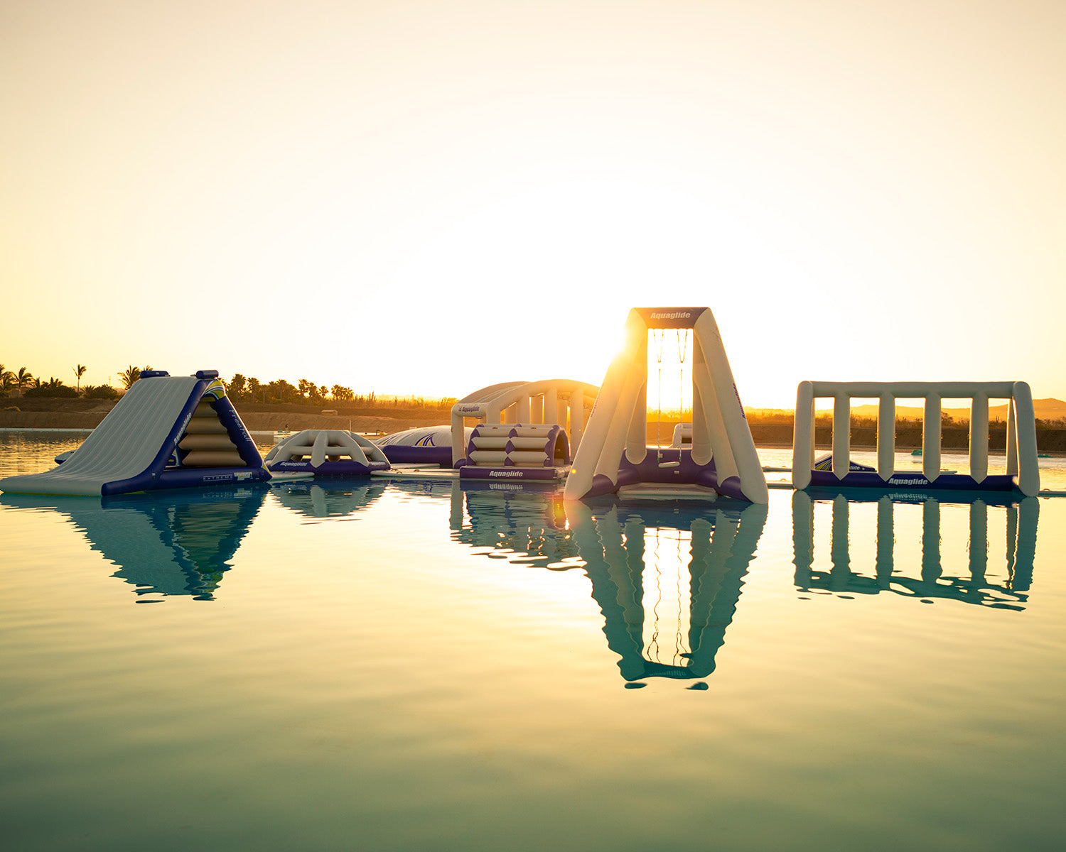 Inflatable water park structures on water at sunset with trees in the background.