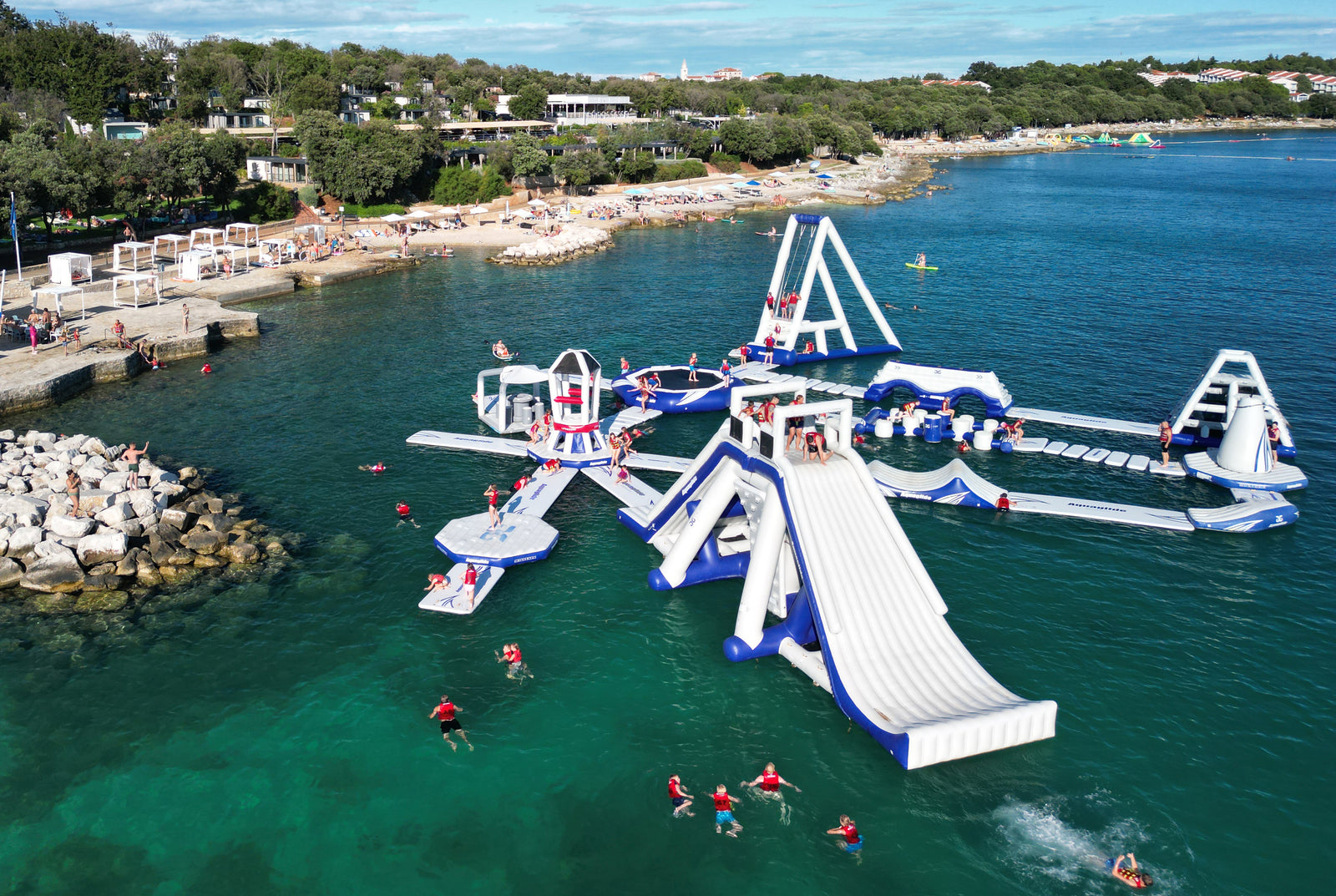 Aquaglide inflatable water park with slides and structures in a body of water near a beach.