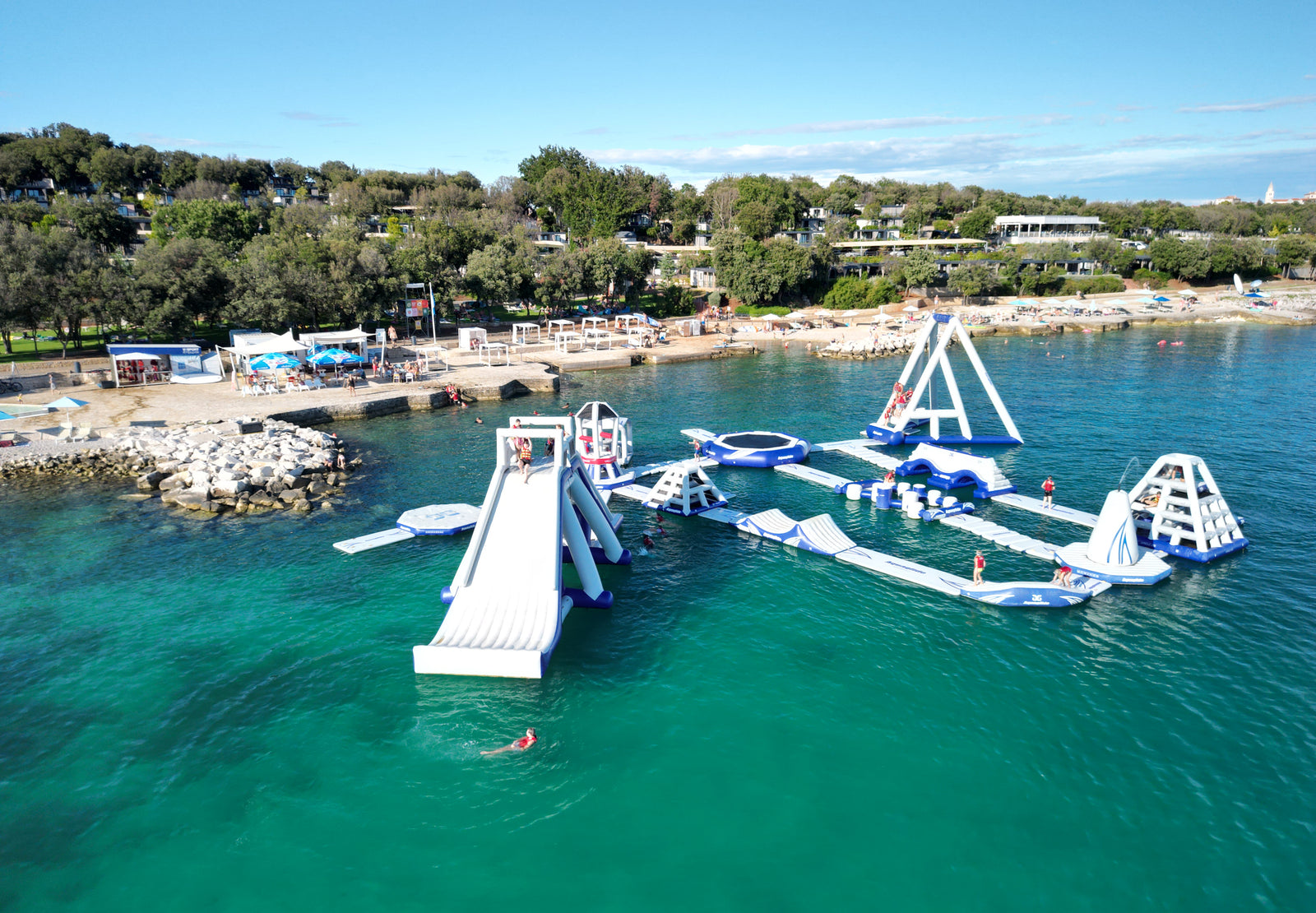 Aquaglide inflatable water park on a body of water with a scenic background.