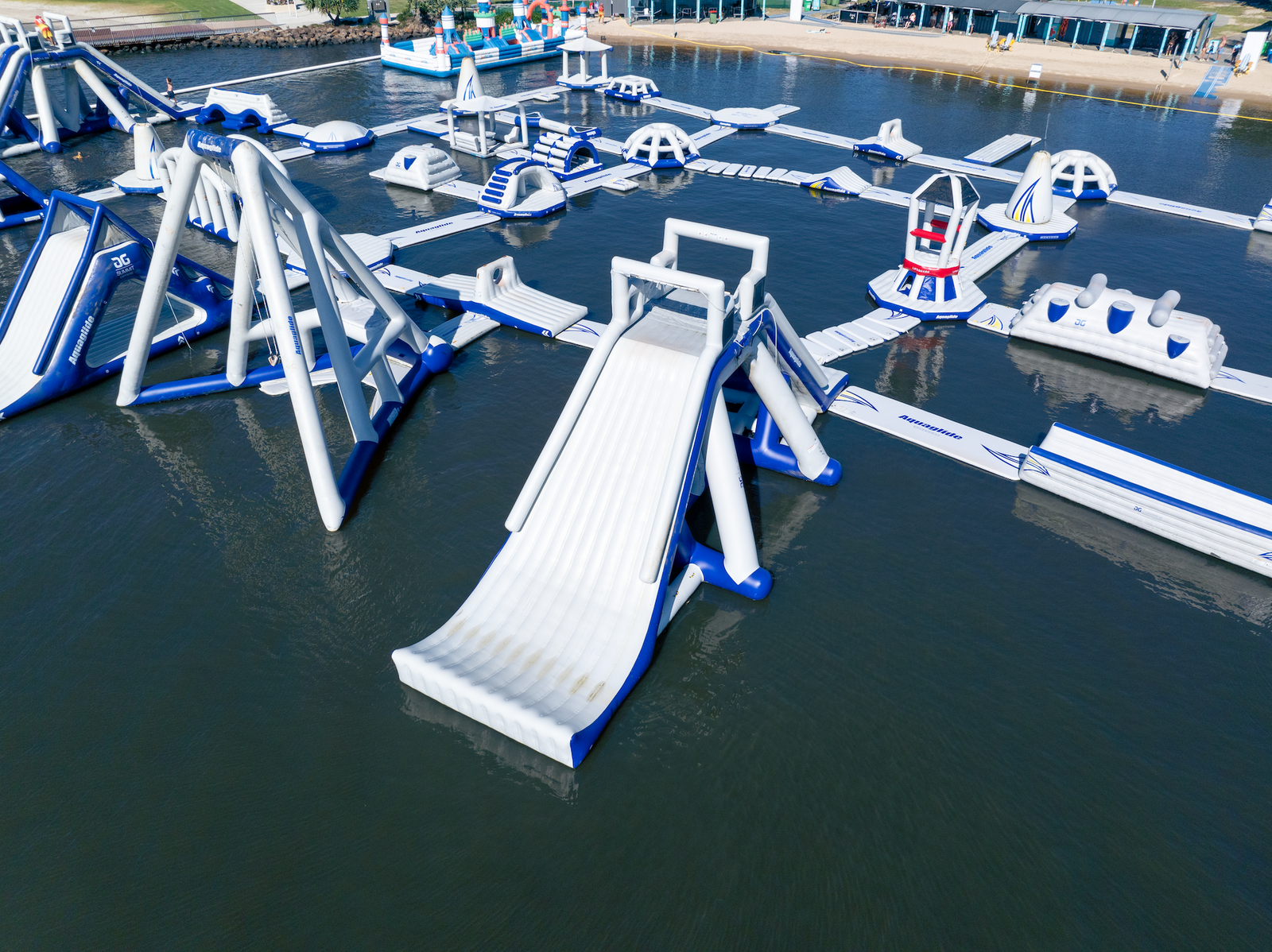Aerial view of Aquaglide water park with inflatable slides and bridges near the shore.