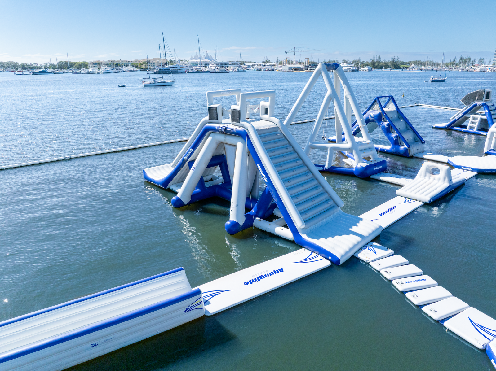 Inflatable Aquaglide slide with ladders and connecting walkways on blue water.