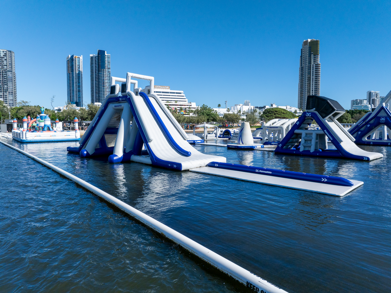 Side view of Aquaglide slides and inflatable path with city buildings in the background.