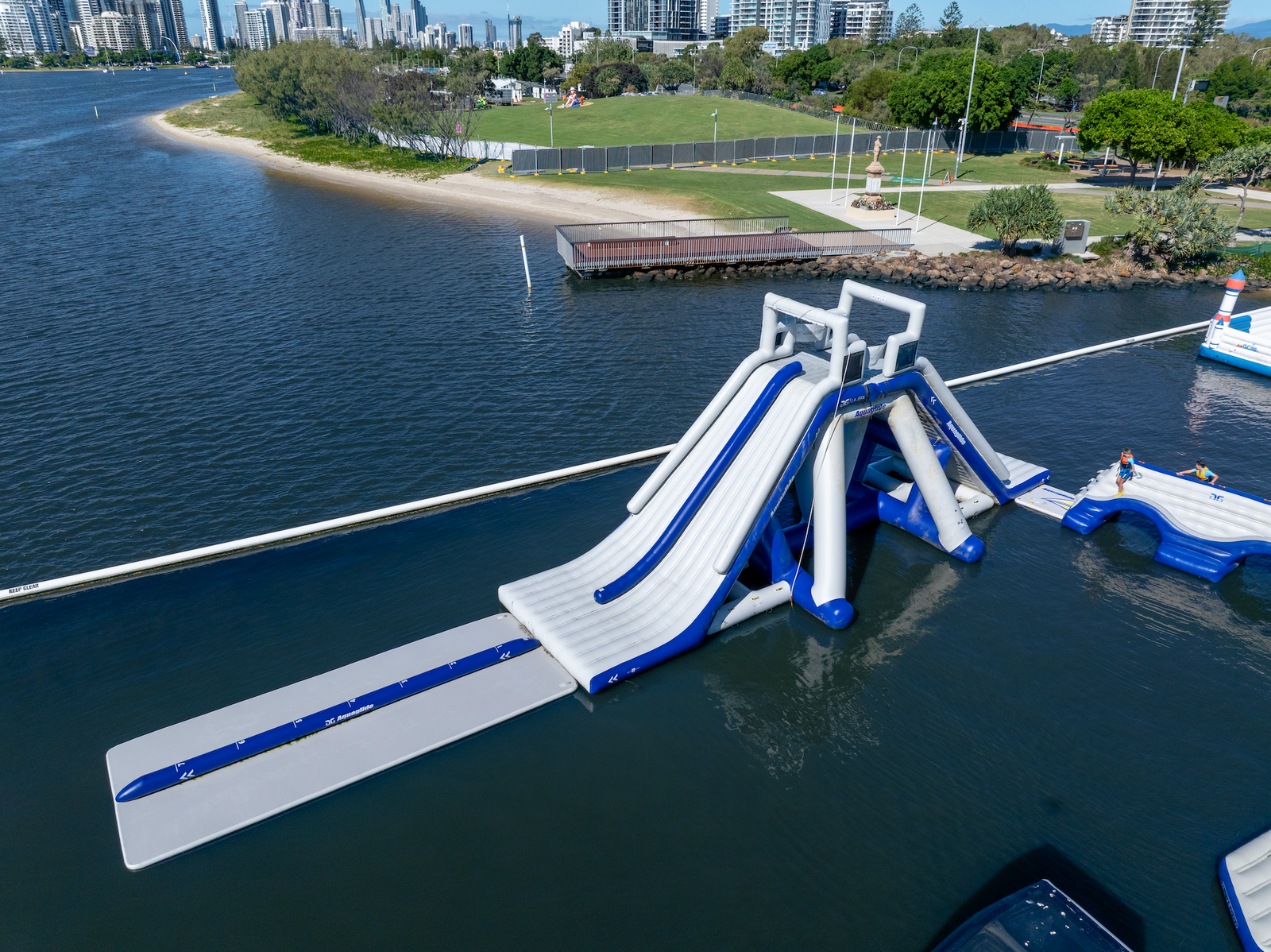 Side view of LA Jefe TR slide with landing pad, set near a city park shoreline.