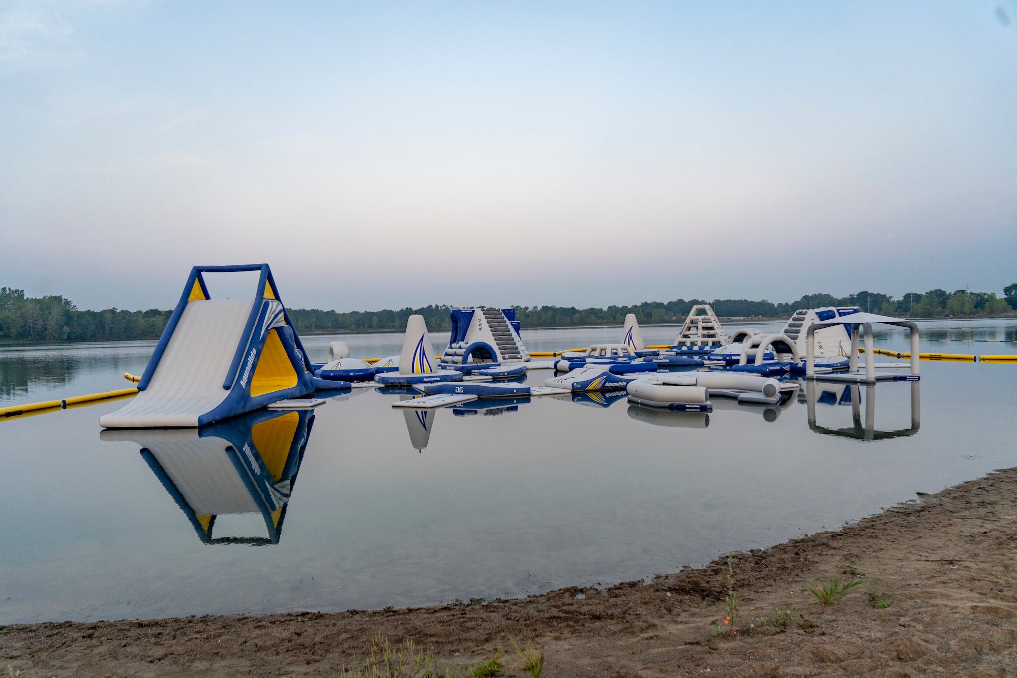 Wide view of Aquaglide water park with slides, towers, and obstacle features on a calm lake.