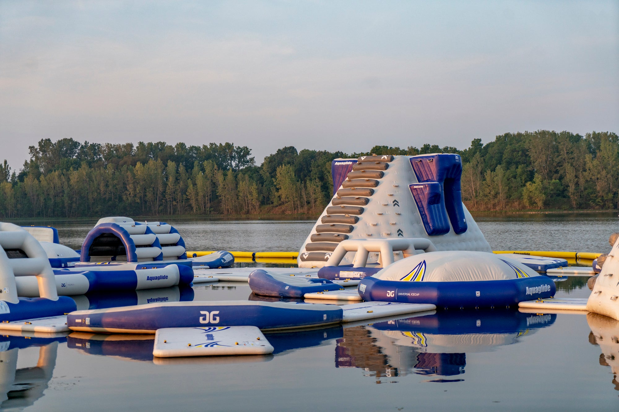 Aquaglide climbing tower and connected floats sit on lake with trees in the background.