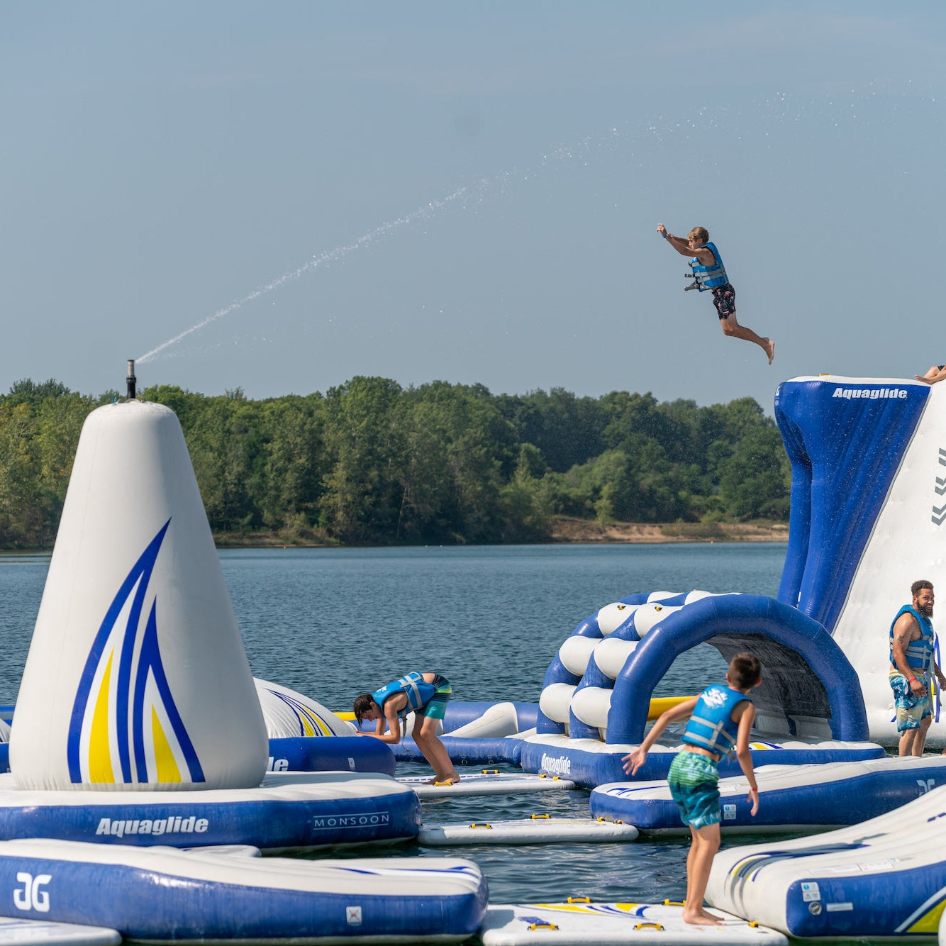 Floating Aquaglide Water park with one kid jumping off the very top jump platform high above his friends.