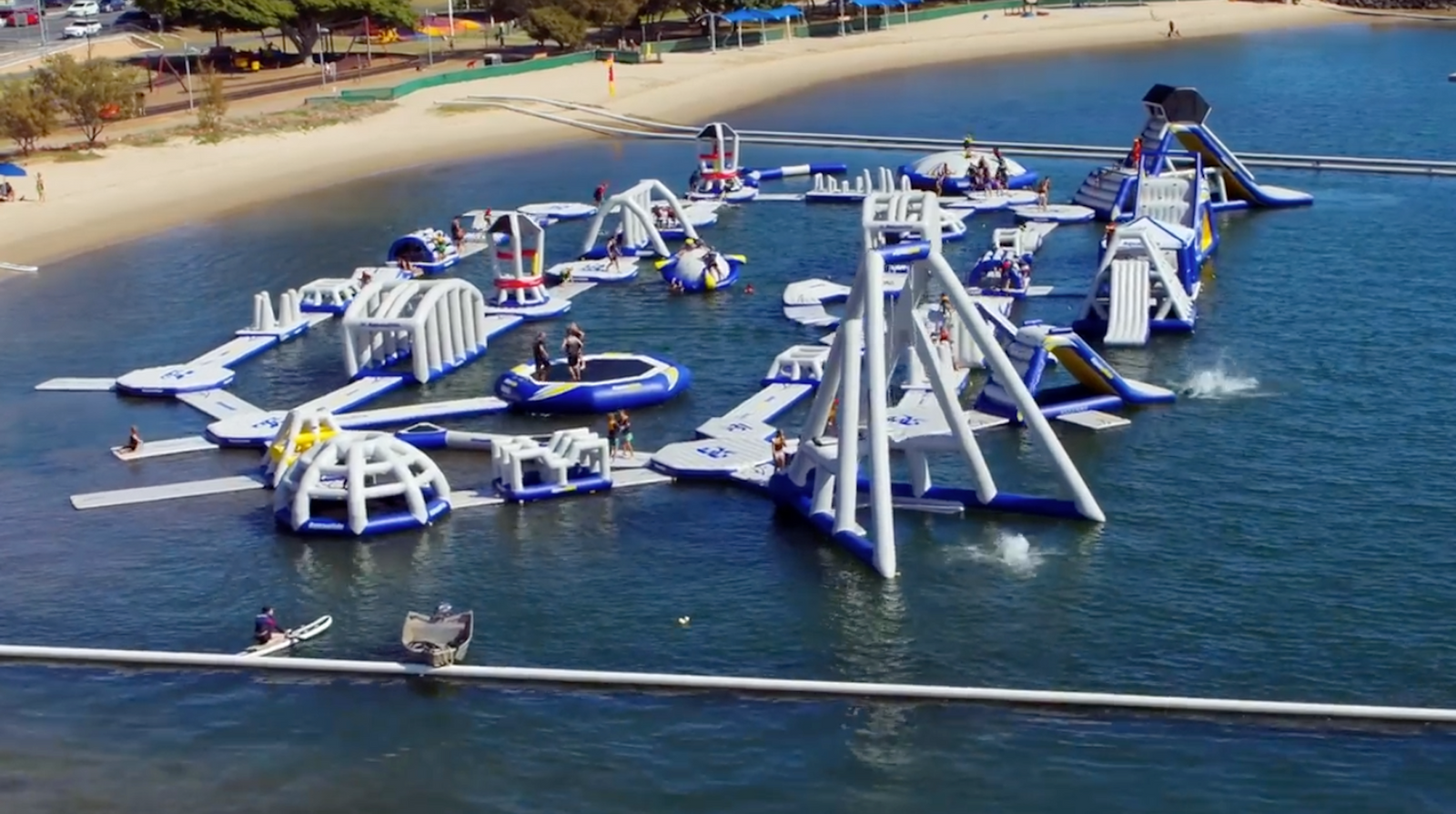 Aquaglide water park filled with slides, towers, and climbers in a busy bay near the beach.