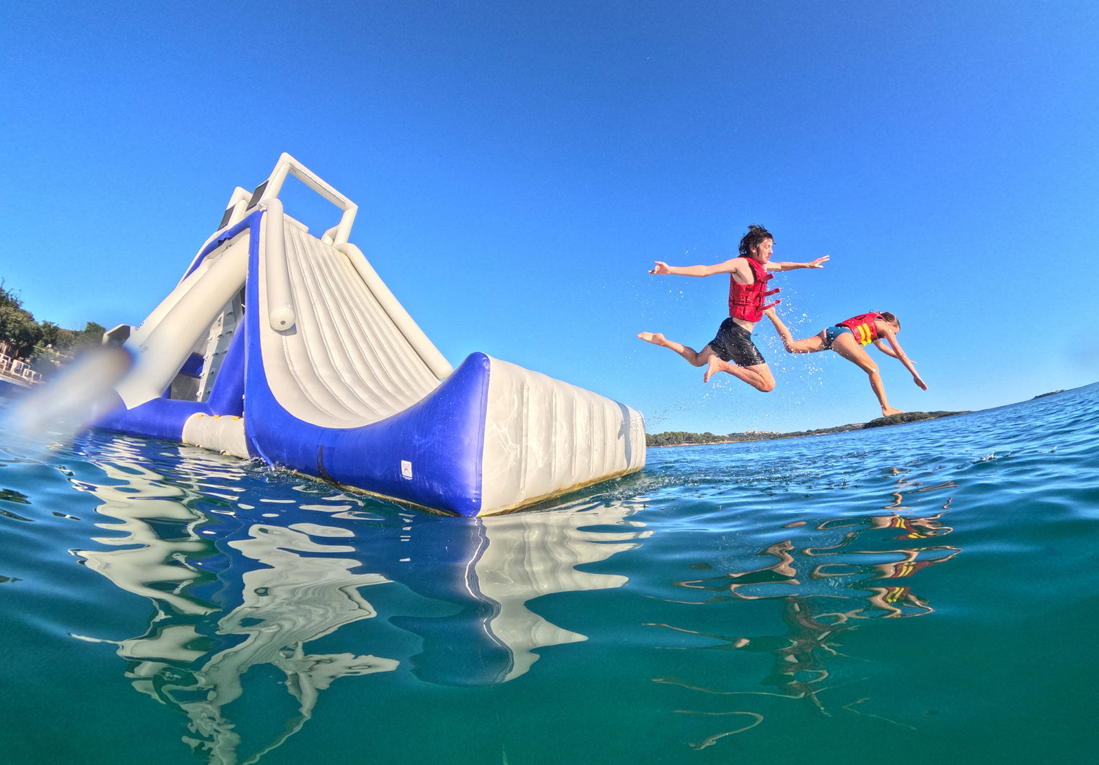 Two people jumping from an inflatable water slide into the water on a clear day.