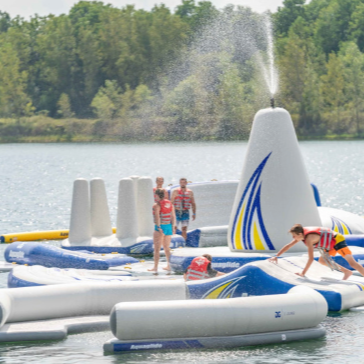 People enjoying an inflatable water park on a sunny day, with trees in the background.