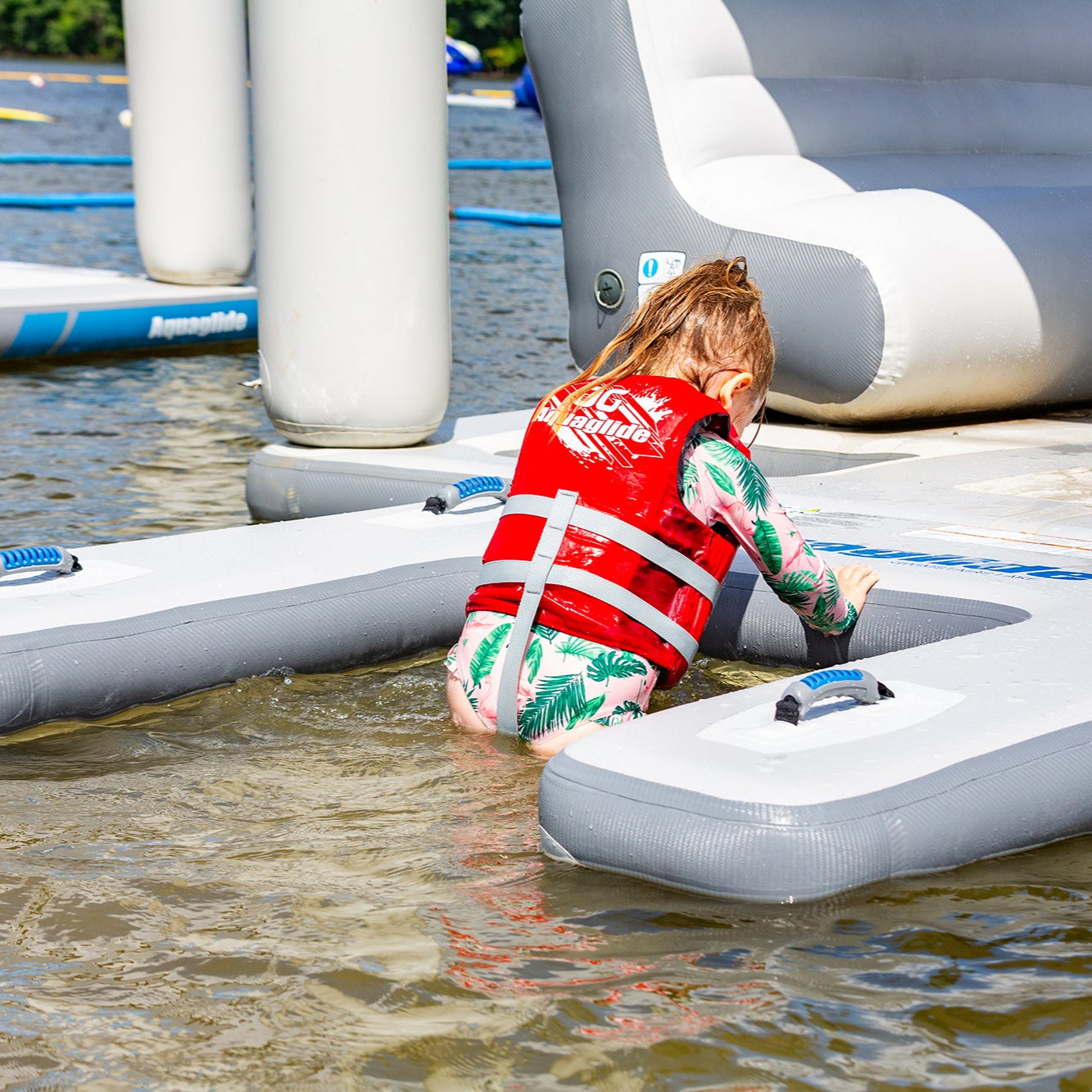 Child in life jacket enjoying Swimstairs XL on an inflatable lake platform.