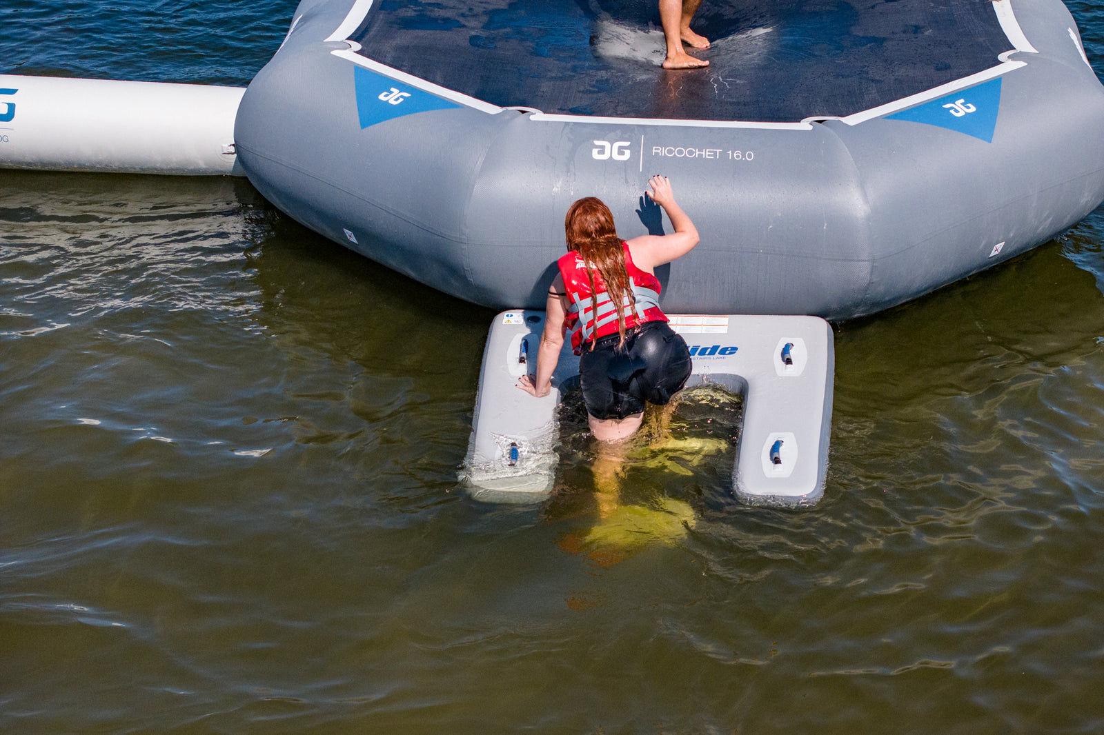 Person boarding Swimstairs Lake water trampoline, wearing a red life jacket.