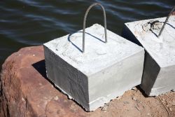 Concrete anchor block with metal lifting handles resting on a dock edge.