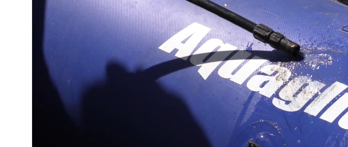 Close-up of a hose spraying water across a blue inflatable surface with white logo.