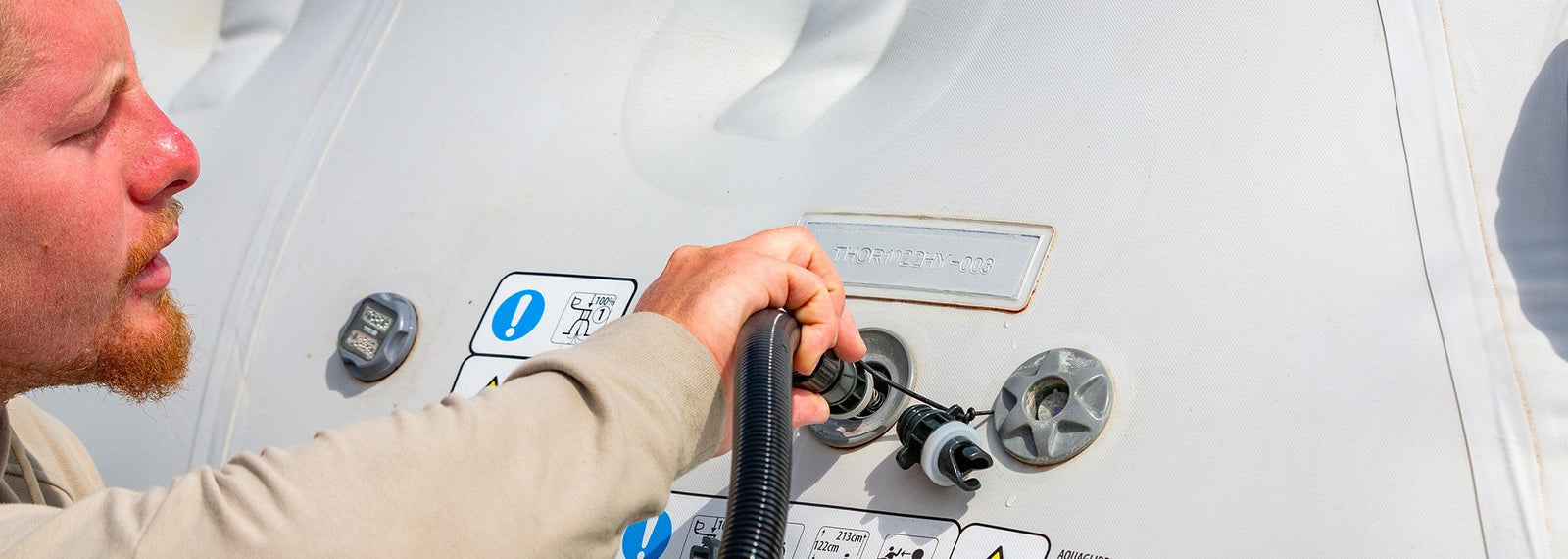 Close-up of a hand connecting an air hose to an inflatable valve port.