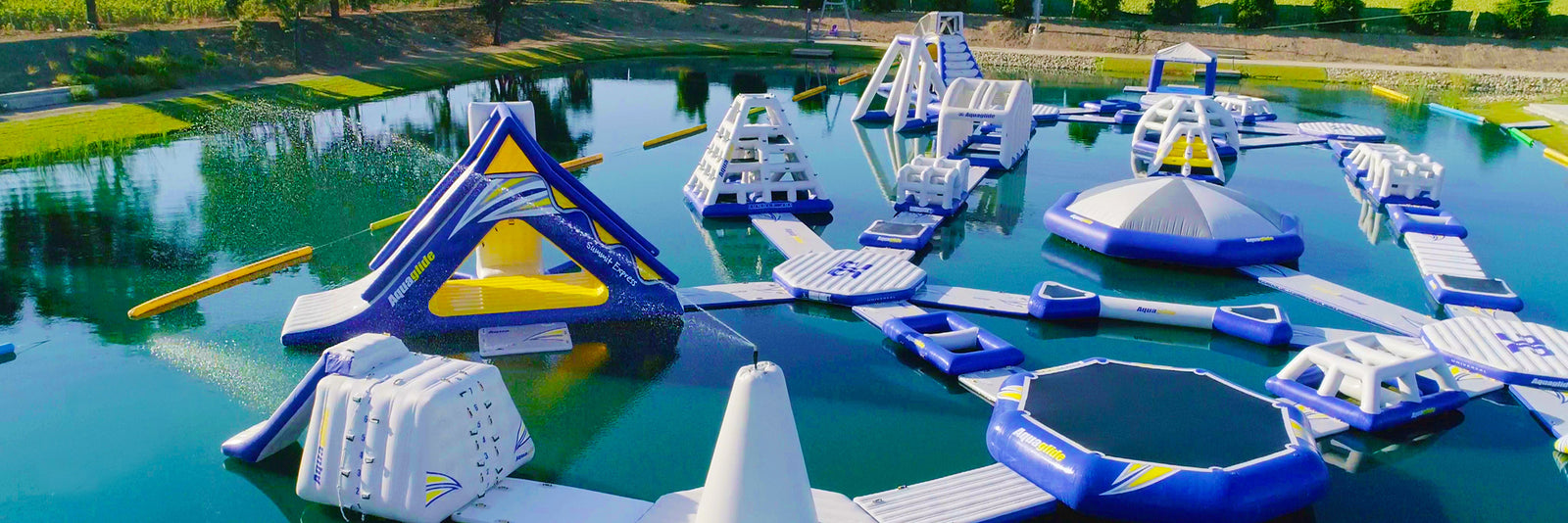 Floating water park on a lake with inflatable slides, obstacles, and a trampoline surrounded by trees.
