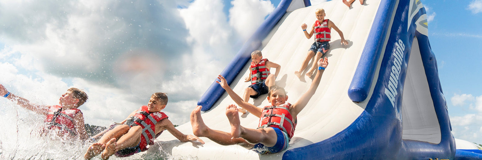 Children in life jackets sliding down a large inflatable water slide, splashing into the water below.