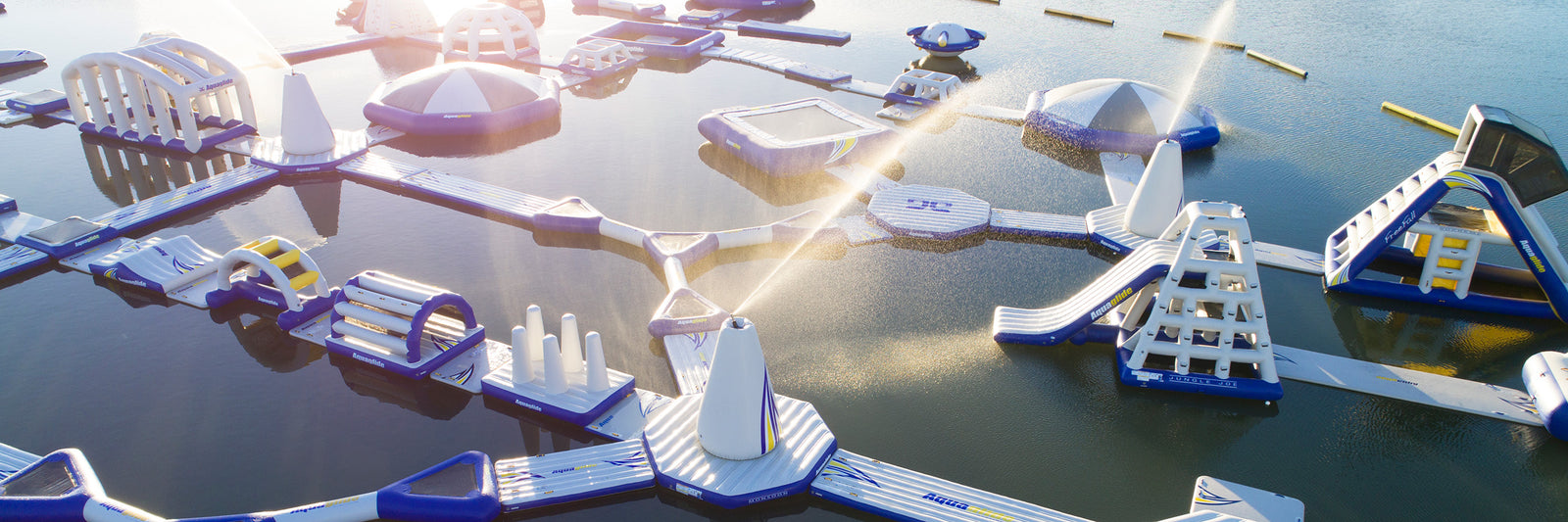 Aerial view of a floating inflatable water park with slides and obstacle courses on a calm lake.