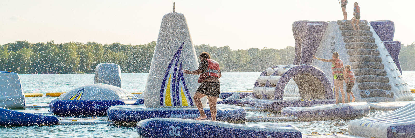 People enjoying an inflatable water park with obstacles and slides on a lake under a clear sky.