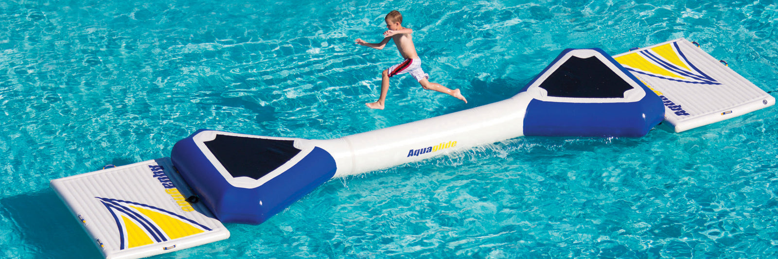 Person running on a floating inflatable obstacle in a pool, surrounded by bright blue water.