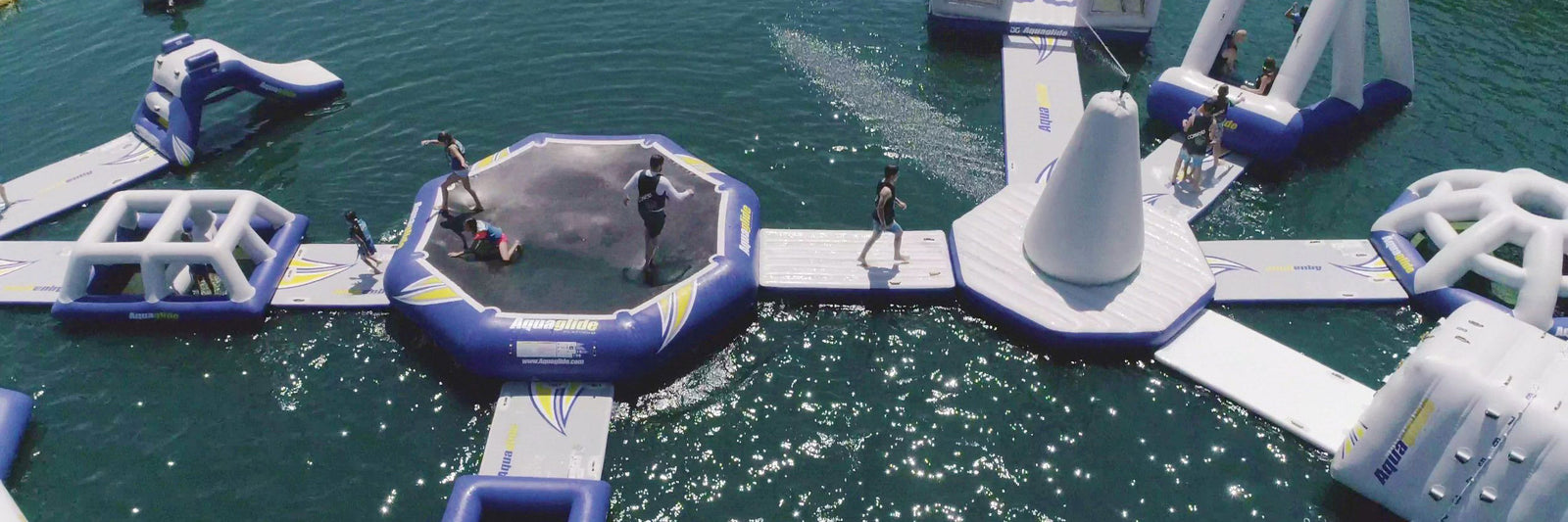 People enjoying an inflatable water park with slides, trampolines, and walkways on a sunny day.