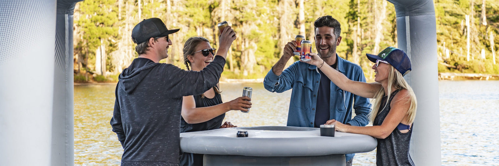 Four people standing at an inflatable bar on a lake, raising cans in a celebratory toast.