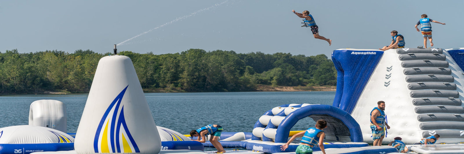 Person jumping off large inflatable water park structure over lake, with others climbing nearby.