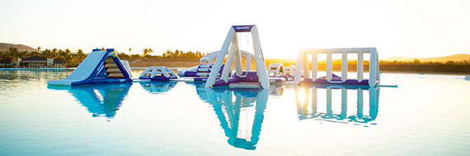 Wide view of inflatable water park with slides and climbing structures reflecting on calm water.