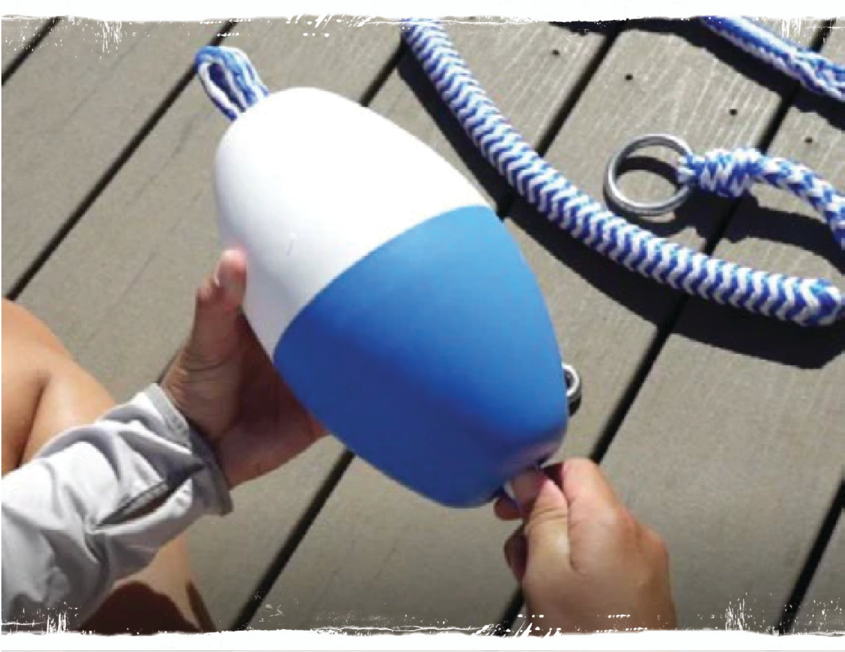 Close-up of hands holding blue and white buoy with attached braided rope on dock surface.
