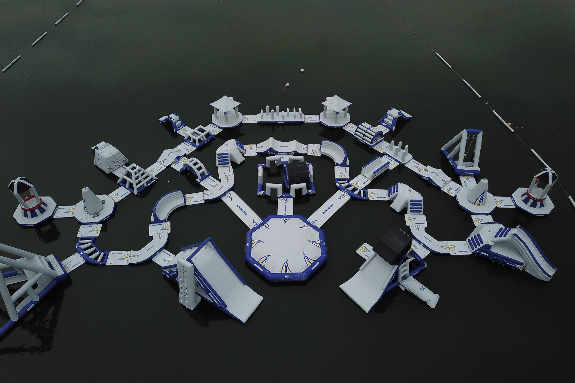 Large inflatable water park with various obstacles on a calm lake.
