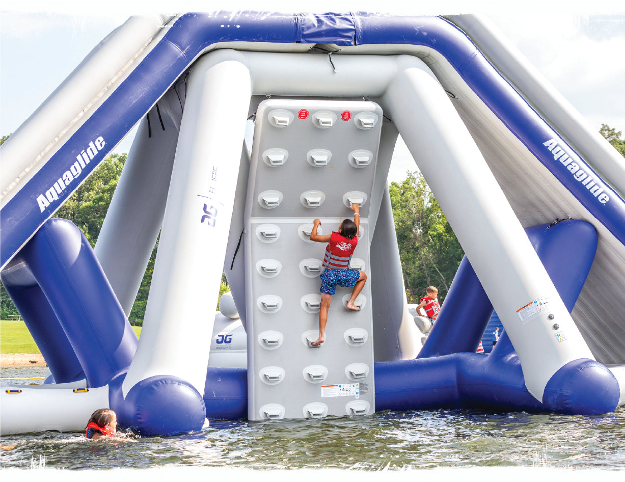 A kid climbing an Aquaglide climing wall on the water