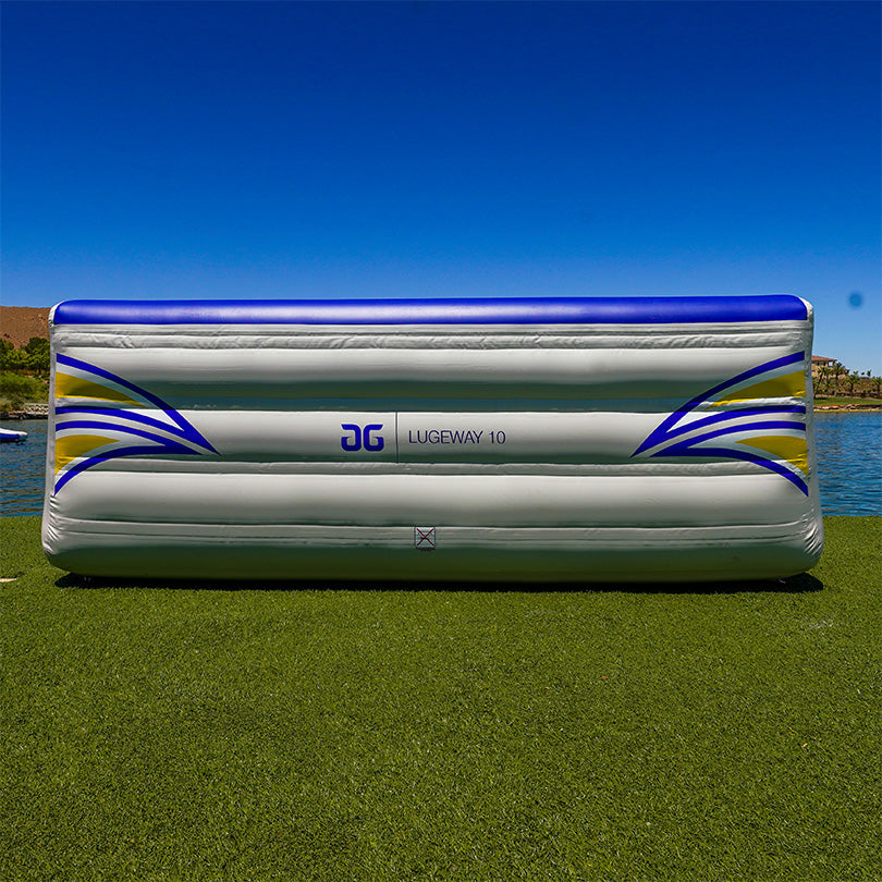 Blue and gray Lugeway 10 inflatable on grass near water under a clear sky, Aquaglide Aquapark.