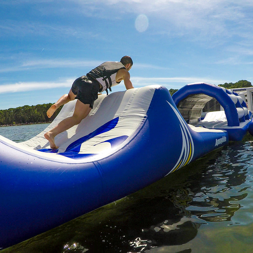 Person climbs a Parkway 30 obstacle course on water under a sunny sky.