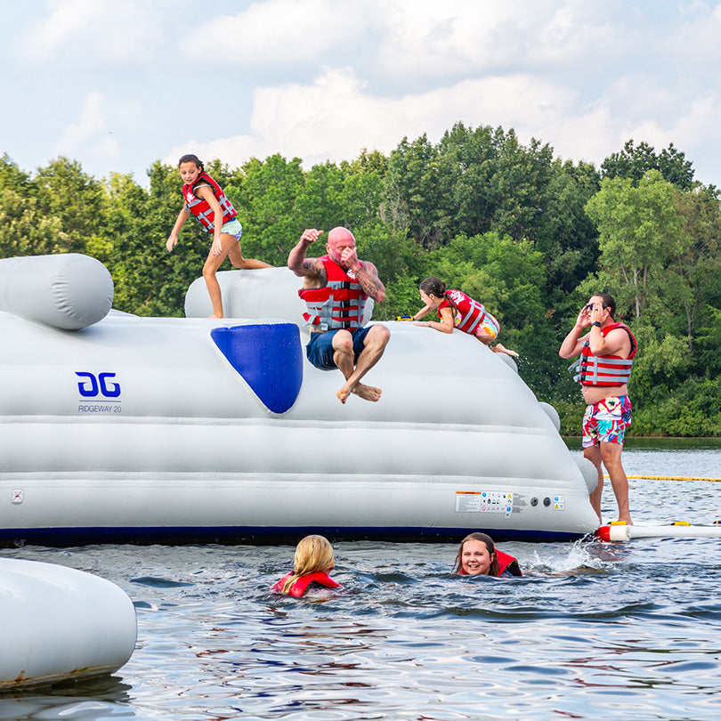 Life-vested people enjoy the Ridgeway 20 inflatable water structure at a lake aquapark.
