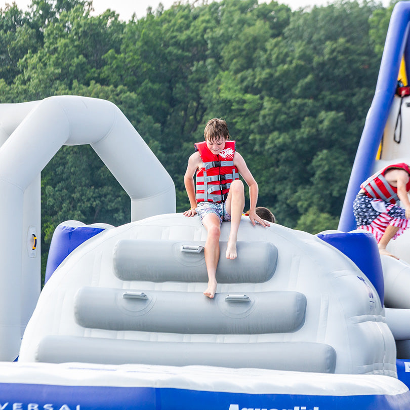 Child in a Ridgeway 10 ascends an aquapark track above water.