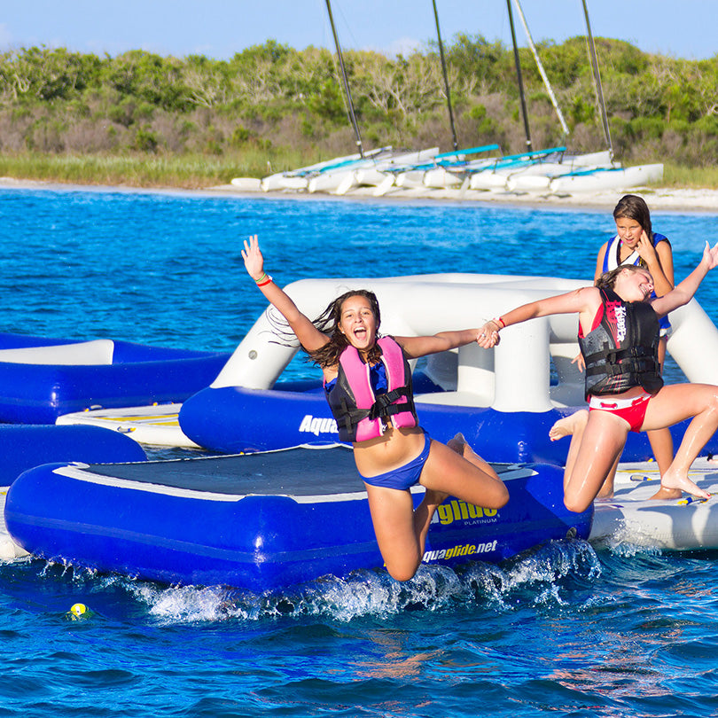 Three people in life jackets jump off a Tango bounce platform into the ocean.