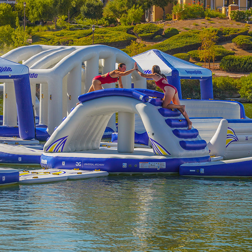 Two people high-five on the Universal Archway slide at a lake.