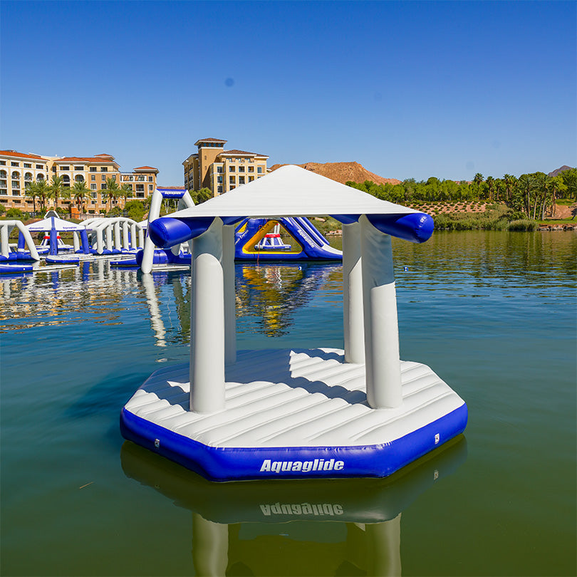 A blue and white inflatable Universal Pavilion floats on a lake.
