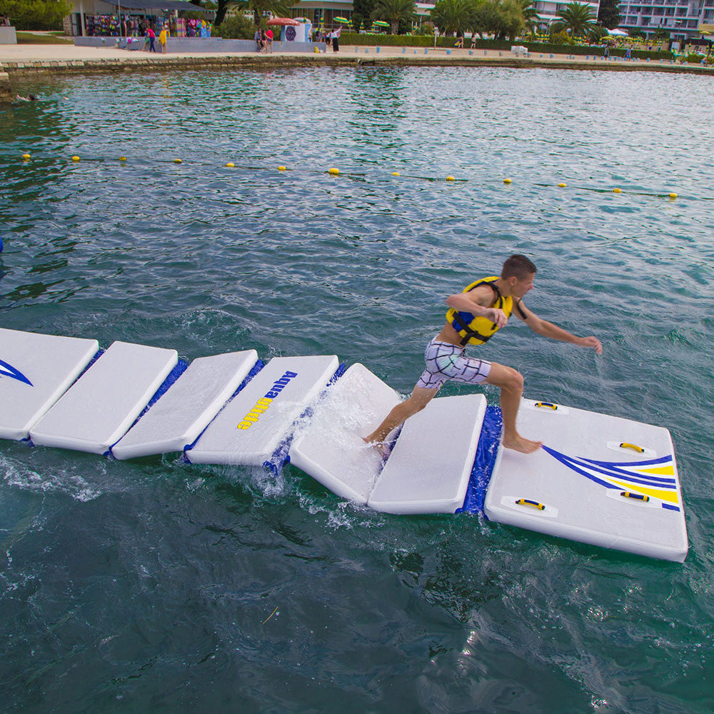 Wearing a life jacket, a person runs on Walk on Water floating mats at an aquapark.