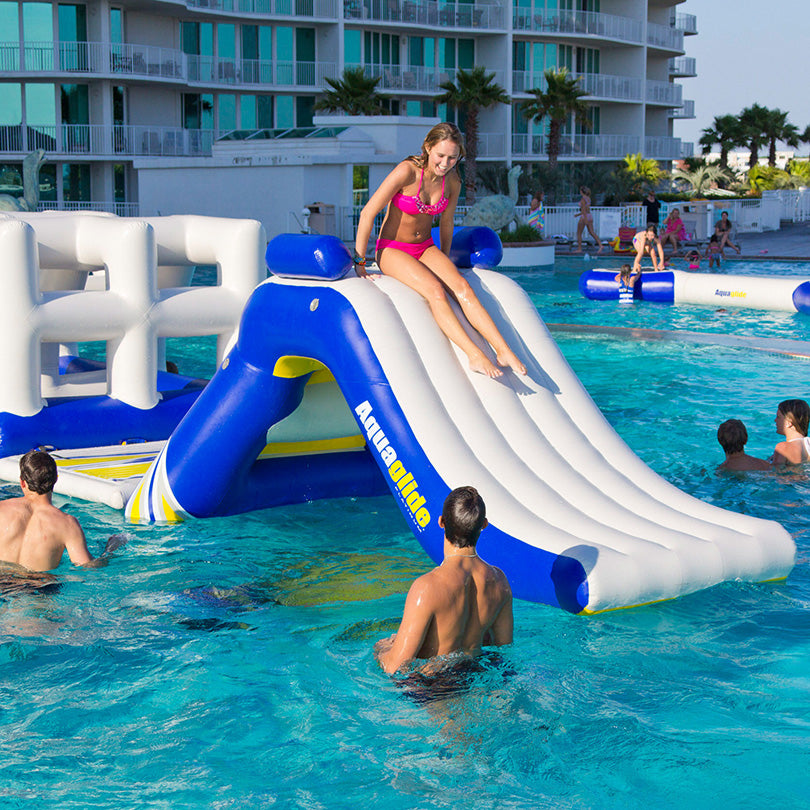 Person slides down the Zulu inflatable slide into a pool; others splash nearby.