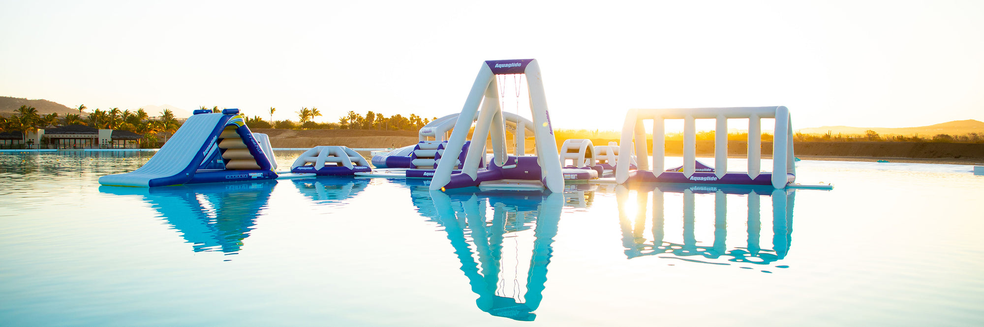 Inflatable water park with slides and obstacles on a calm lake at sunset.