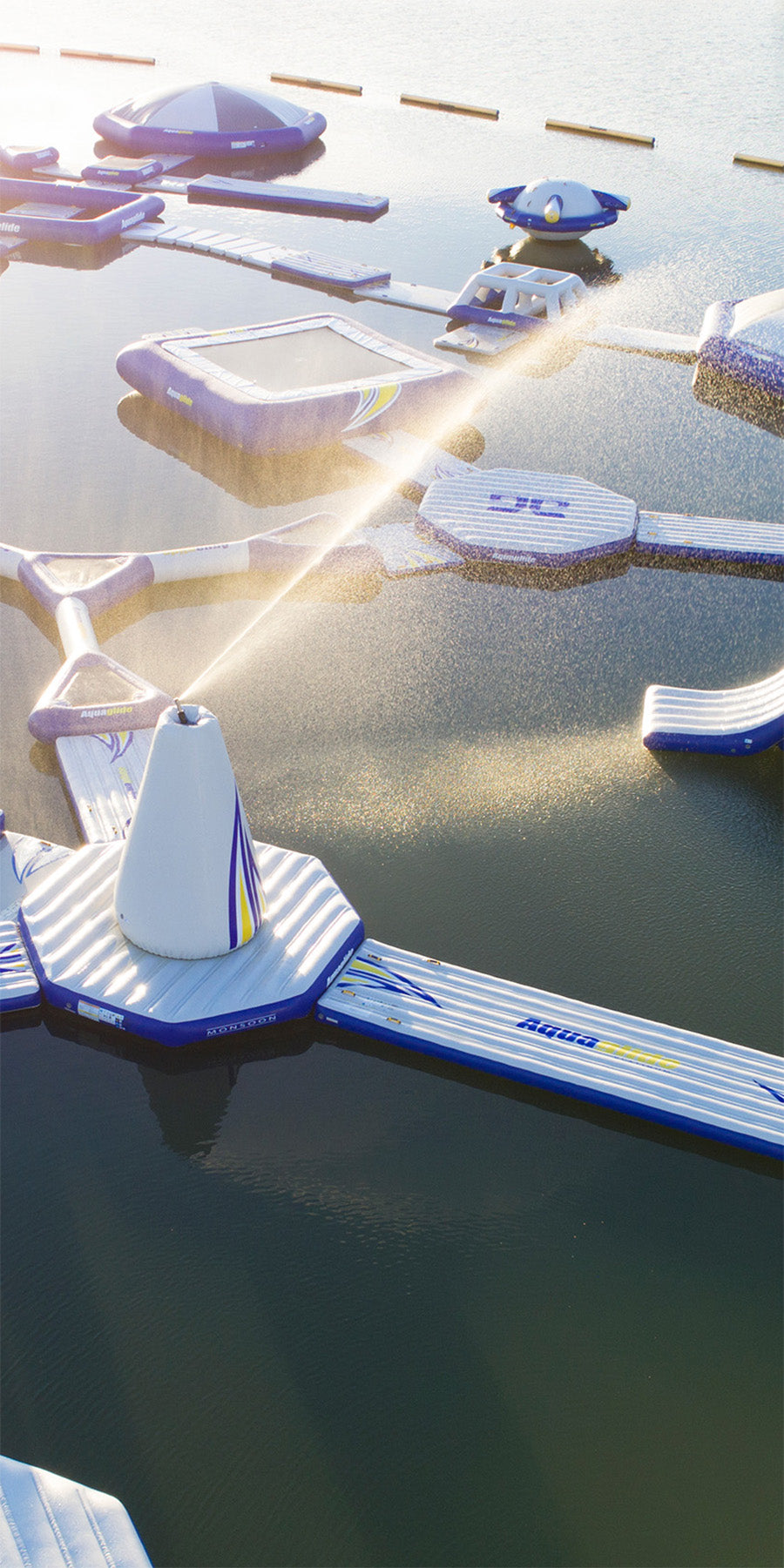 Floating aqua park with inflatable platforms and a fountain spraying water.