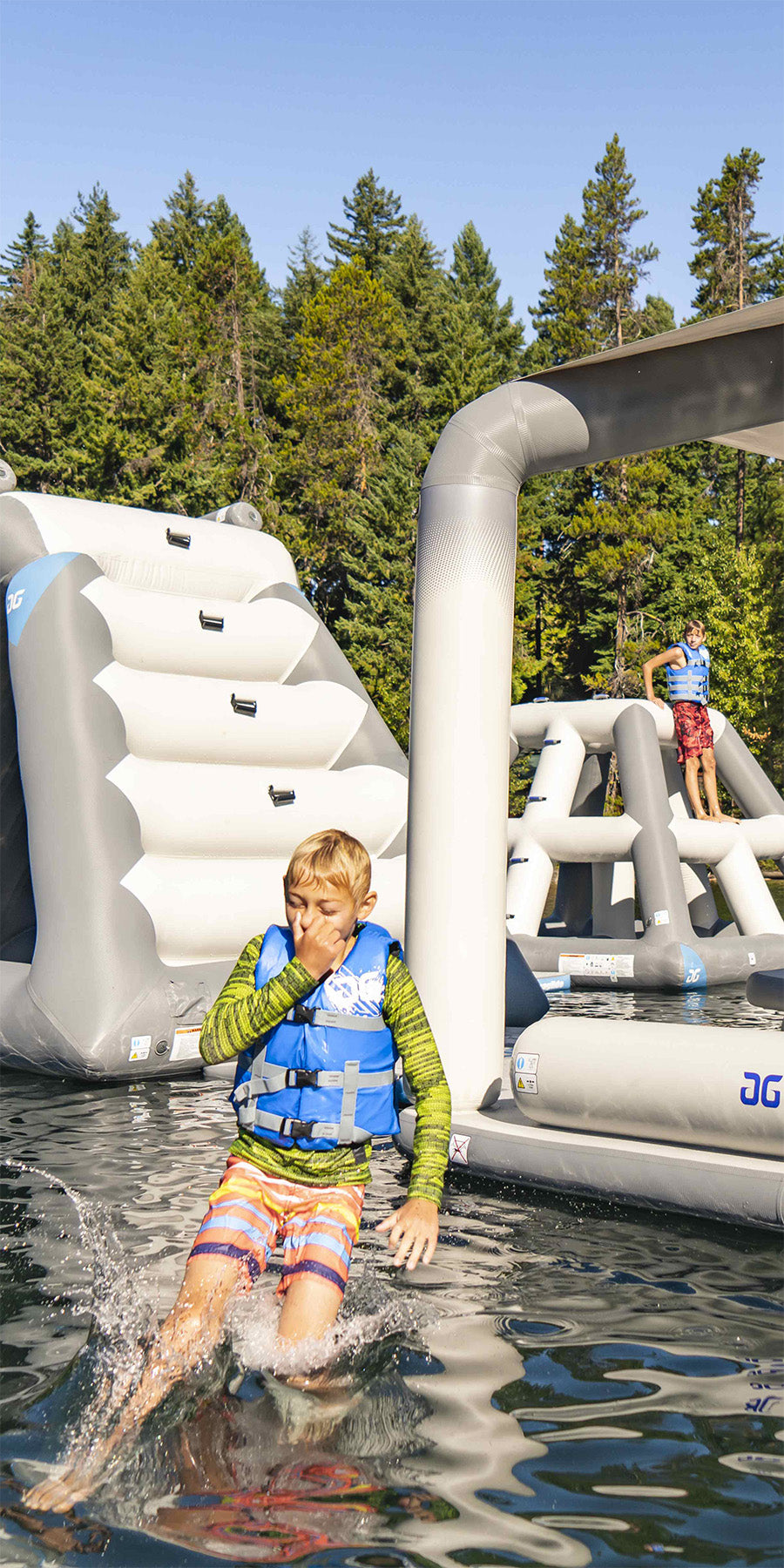 Boy in life vest splashes into water from inflatable, with trees in the background.