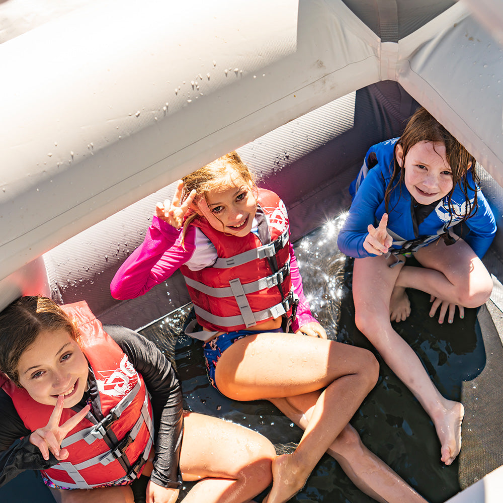 Three kids in life jackets flash peace signs aboard a Lakefront Mini Park 2 inflatable boat.
