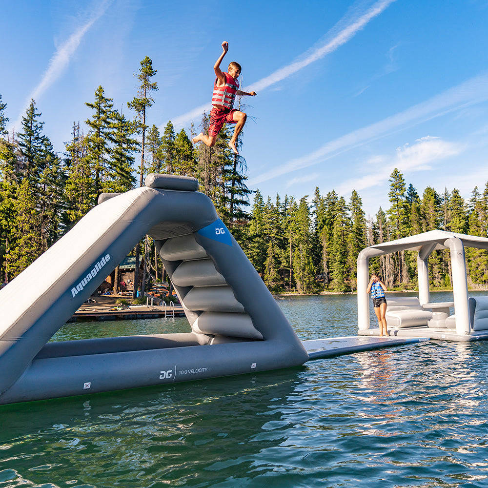 Child jumping off Aquaglide into a lake, another child standing nearby at Lakefront Mini Park 4.